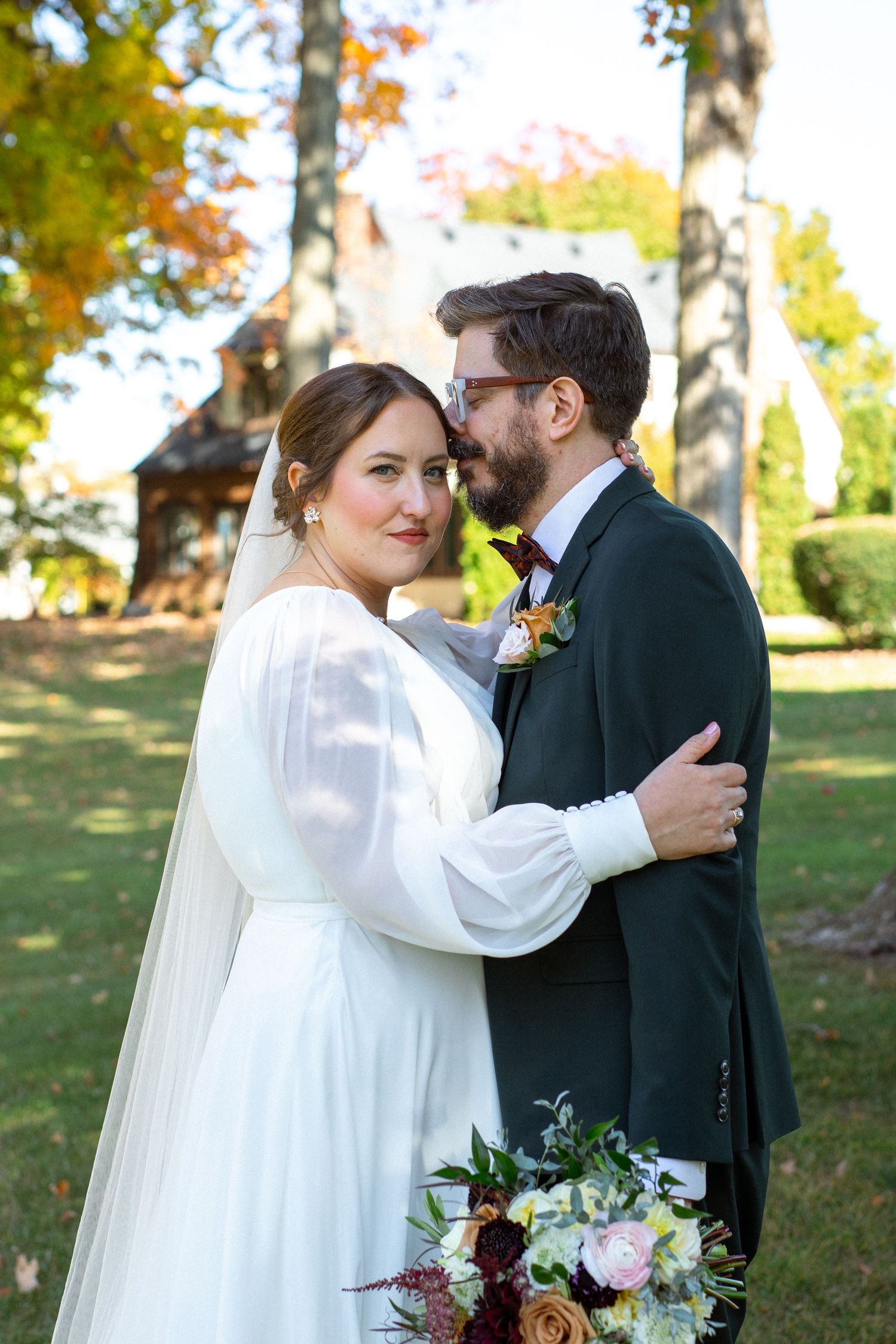 A couple shares an intimate moment outdoors during an autumn wedding ceremony with fall foliage in the background.