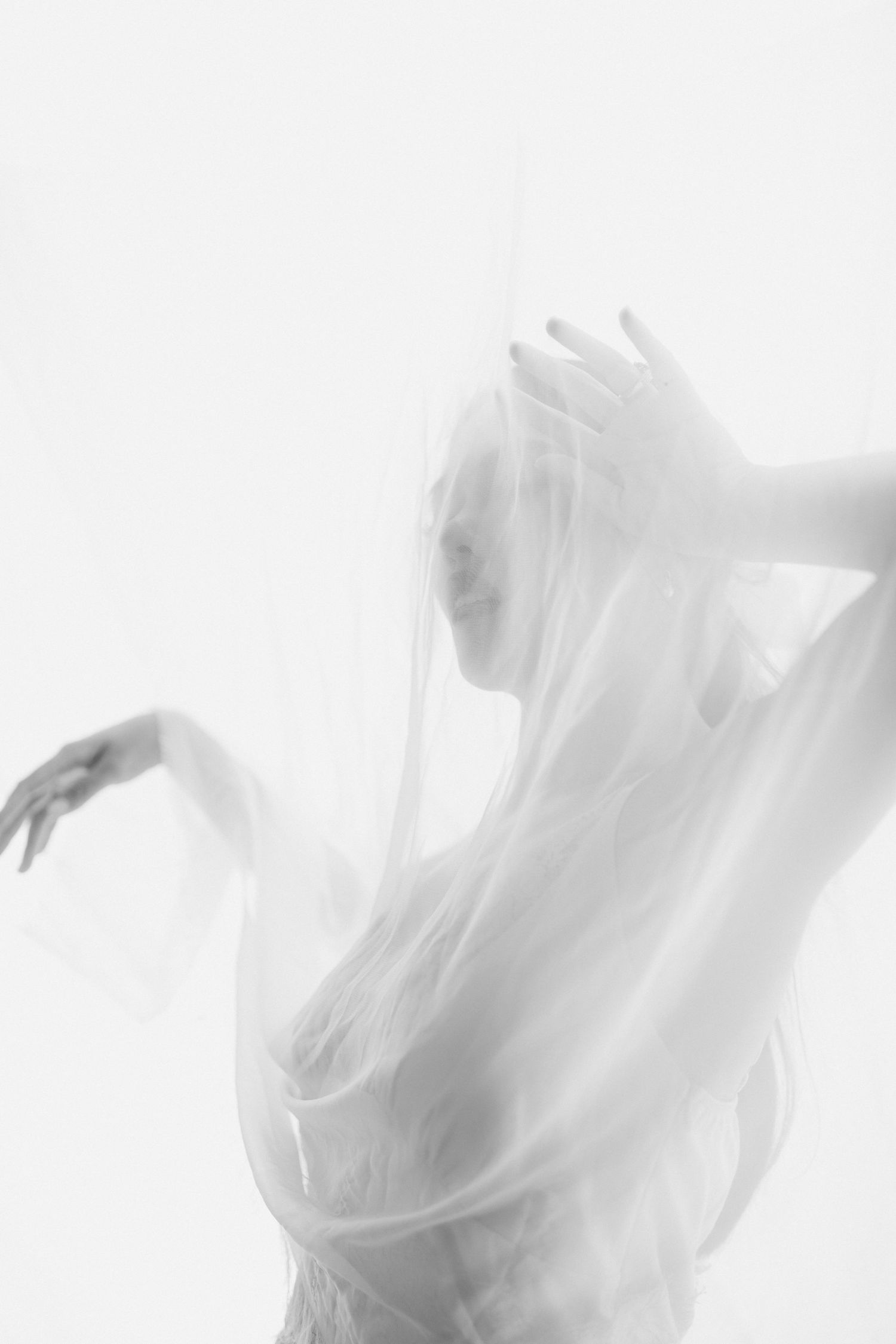 Ethereal silhouette of a figure draped in flowing white fabric creates a dreamy, artistic composition against light background.