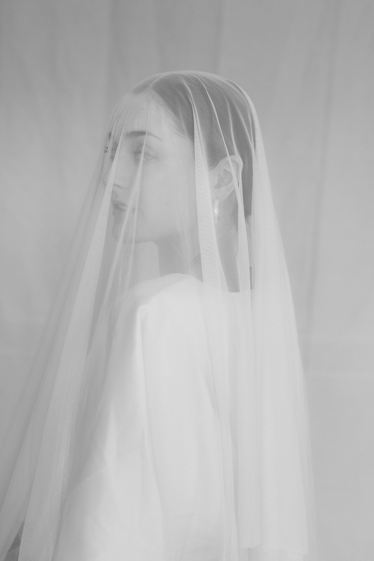 A dreamy black and white portrait of a figure in a delicate bridal veil with soft, ethereal lighting.