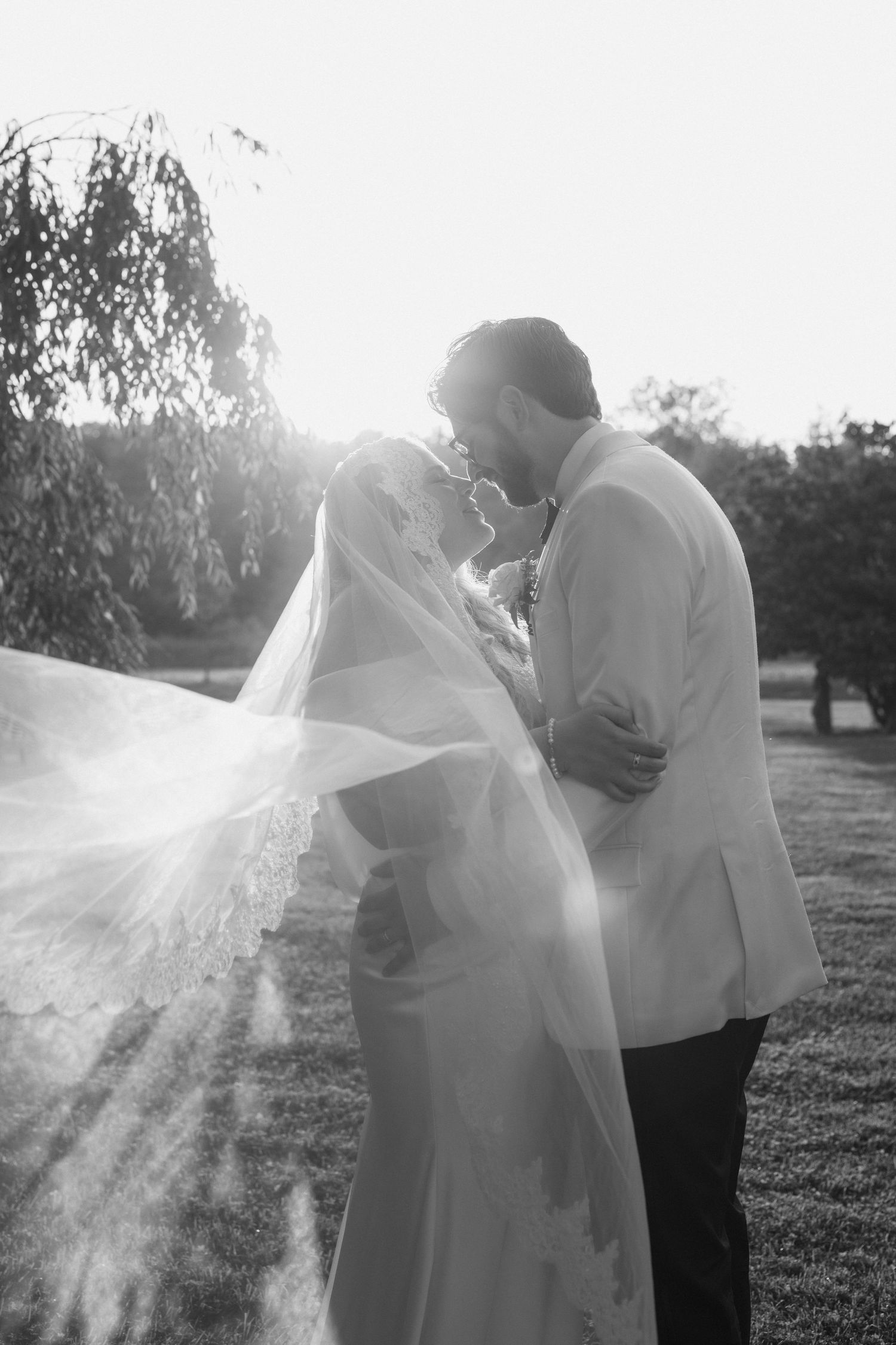 A romantic couple embraces in a sun-drenched outdoor setting as a flowing white veil creates an ethereal effect.