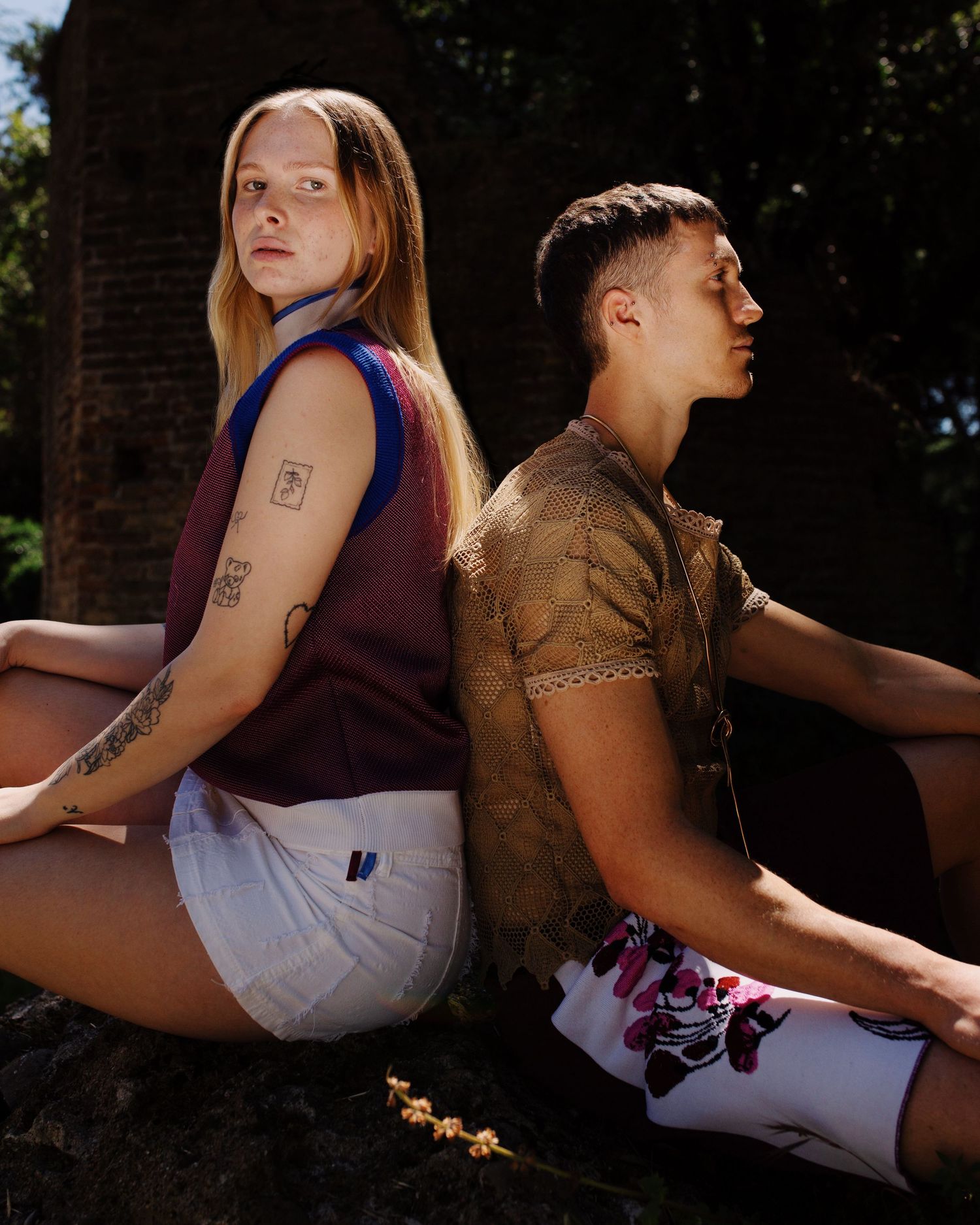 Photograph of a girl and a boy seating back to back on a rock. Photography by studio sale.