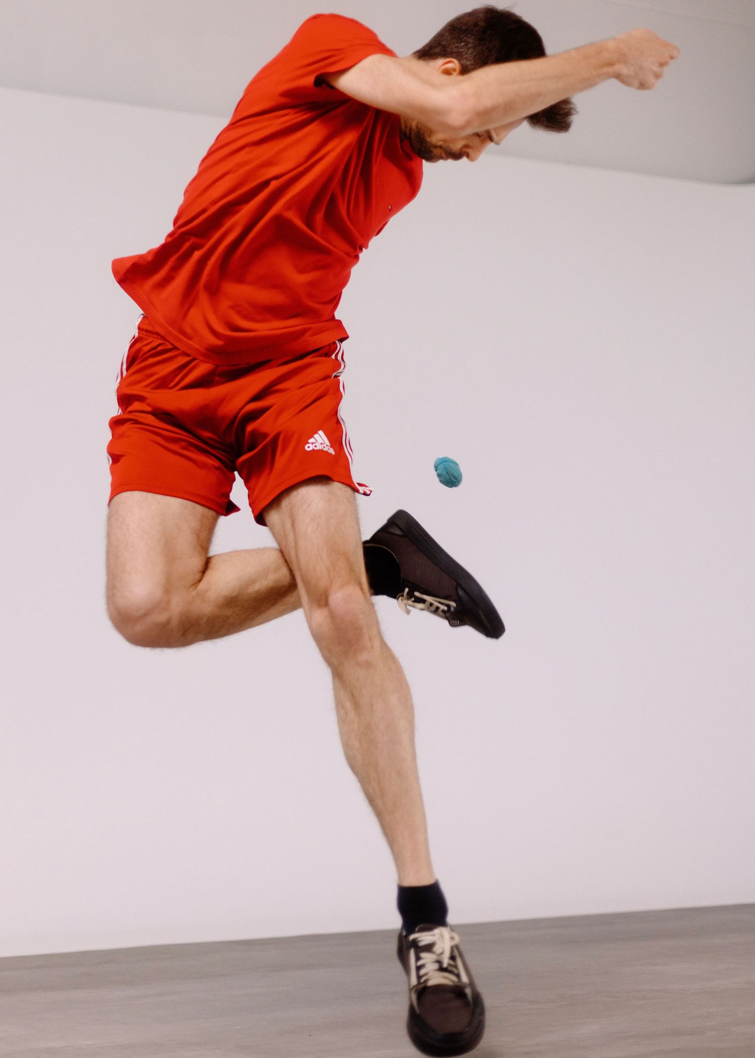 Un ragazzo vestito di rosso gioca allo sport footbag in una sala posa con un limbo bianco ed un pavimento grigio.