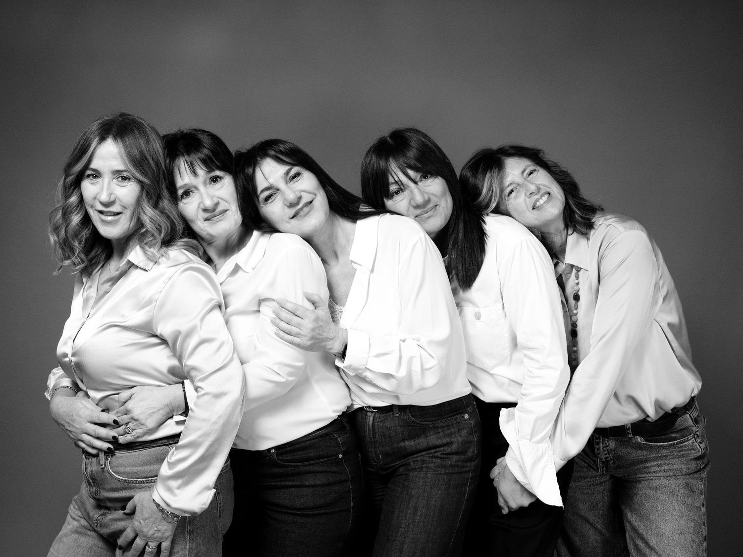 Cinque amiche adulte che si abbracciano indossando delle camicie bianche.
