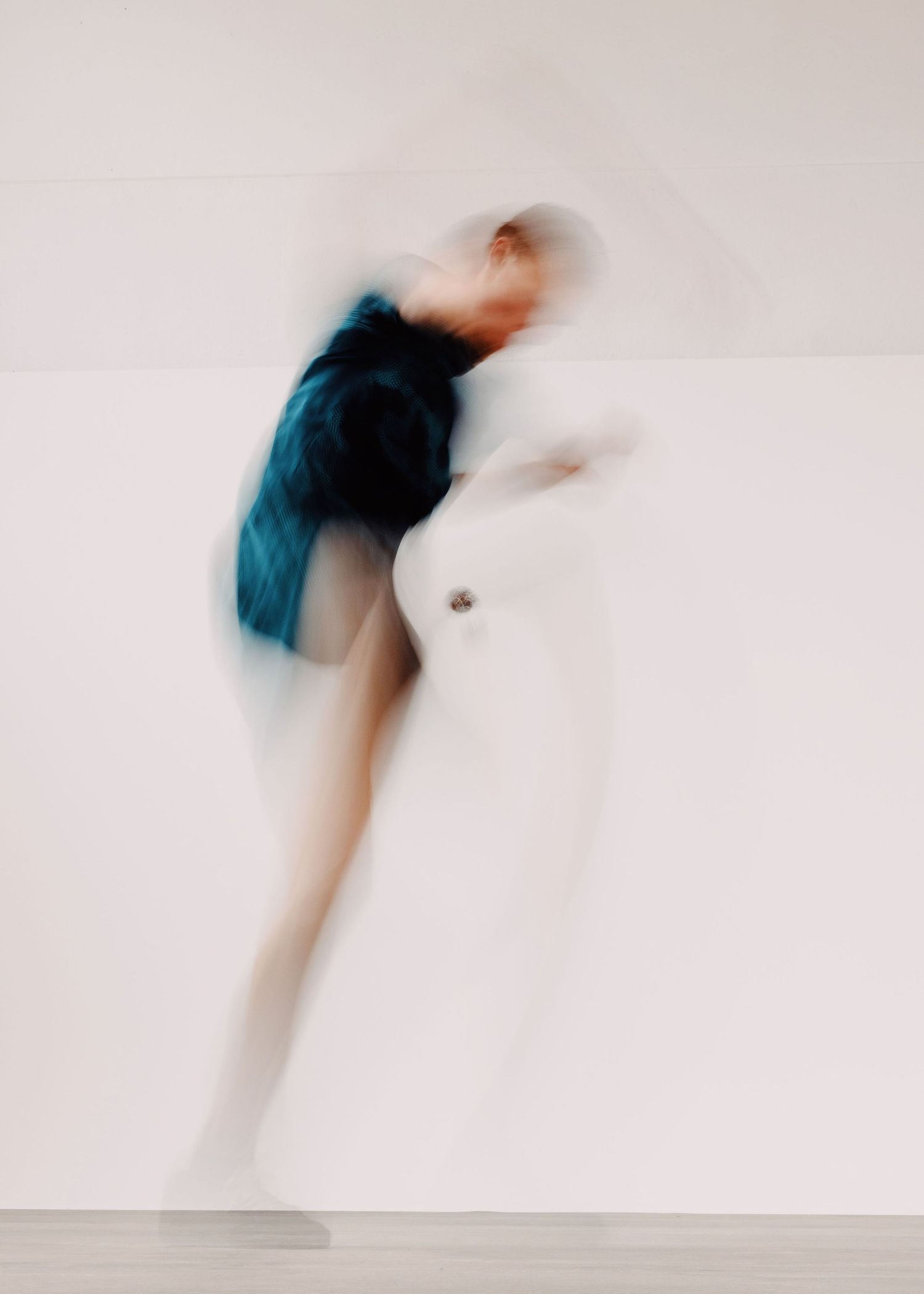 Un ragazzo vestito di blu gioca allo sport footbag in una sala posa con un limbo bianco ed un pavimento grigio.