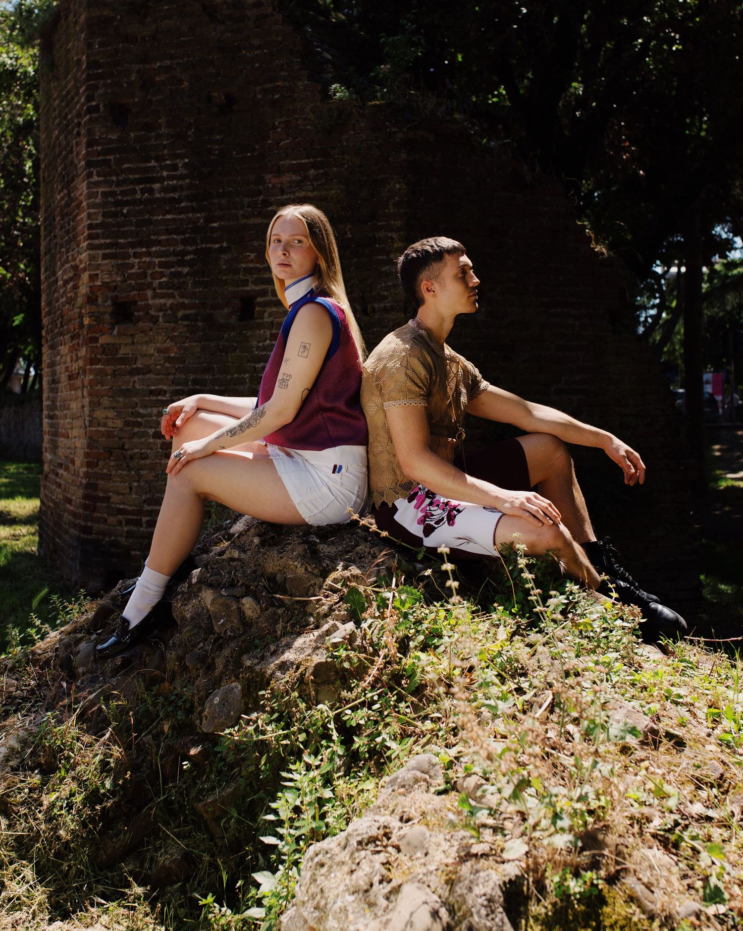 Photograph of a girl and a boy seating back to back on a rock. Photography by studio sale.