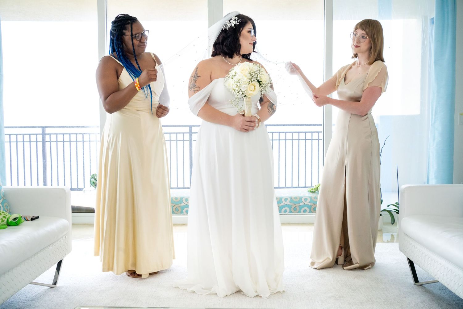 Bride and bridesmaids adjusting bride's head cover in bohemian blue and white condo living room.