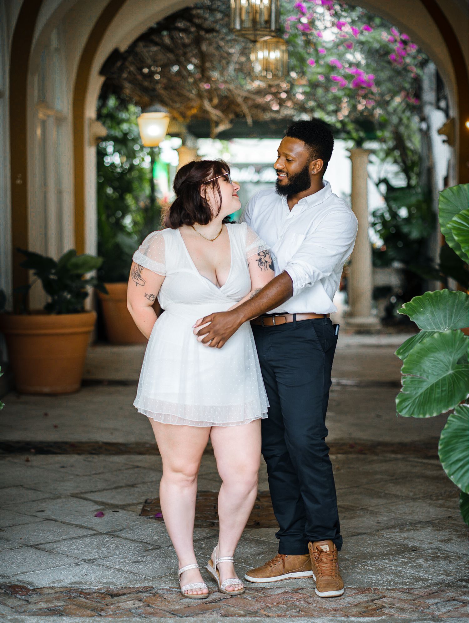 Couple gazing into each other's eyes at a flower-lined walkway at Palm beach island. Upscale architecture, plants, and bright flowers.