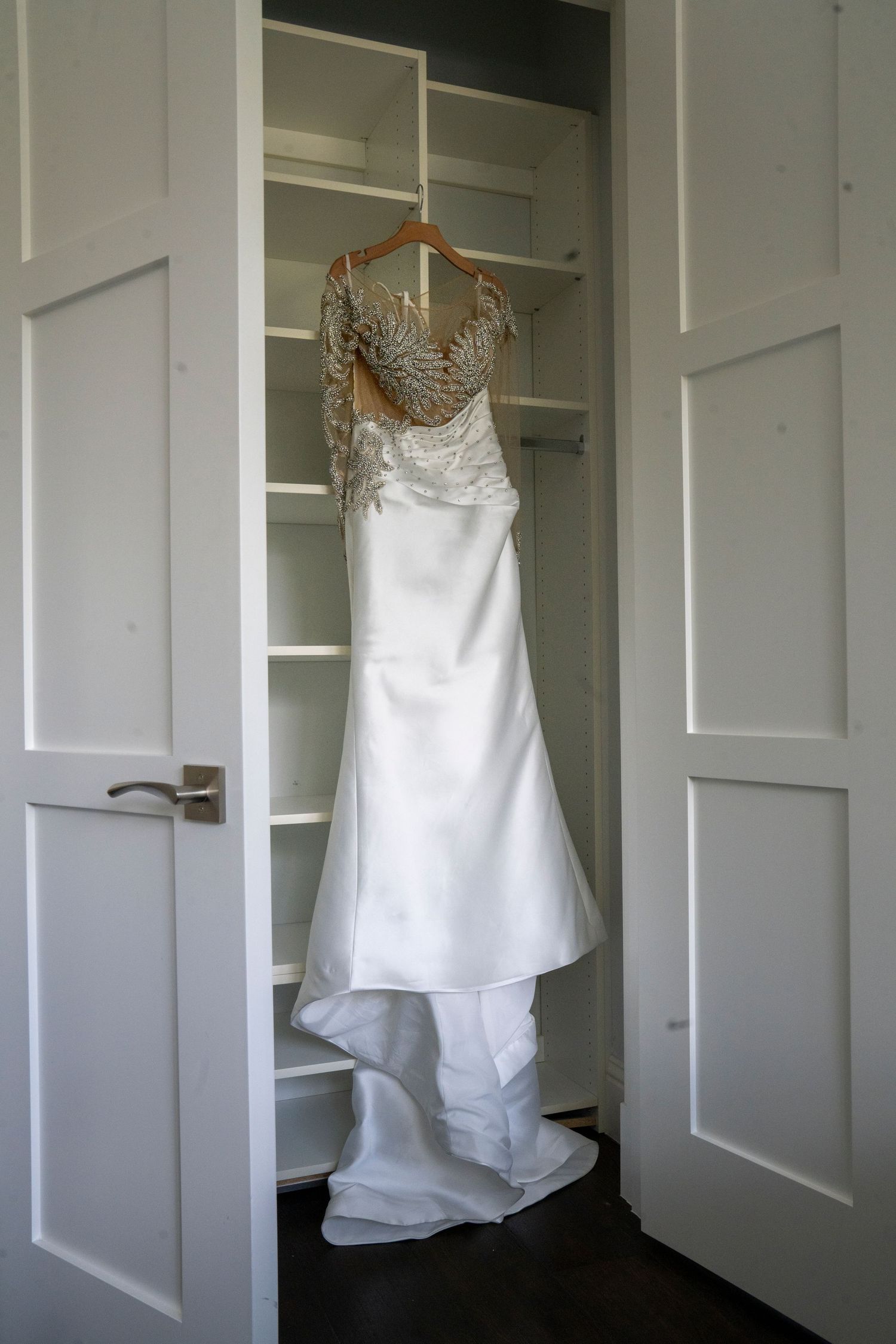 White bedazzled wedding dress hangs in closet while doors open up to reveal.