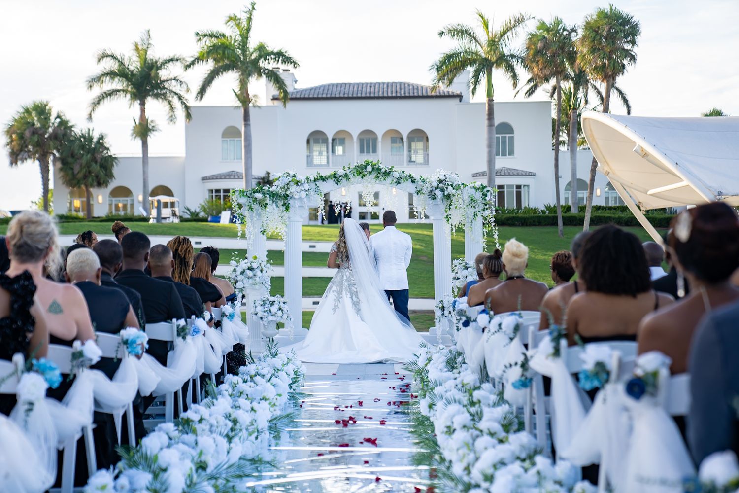 Wedding ceremony. Perspective from behind as audience watches bride and groom get married outdoors with tuckahoe mansion in the background.