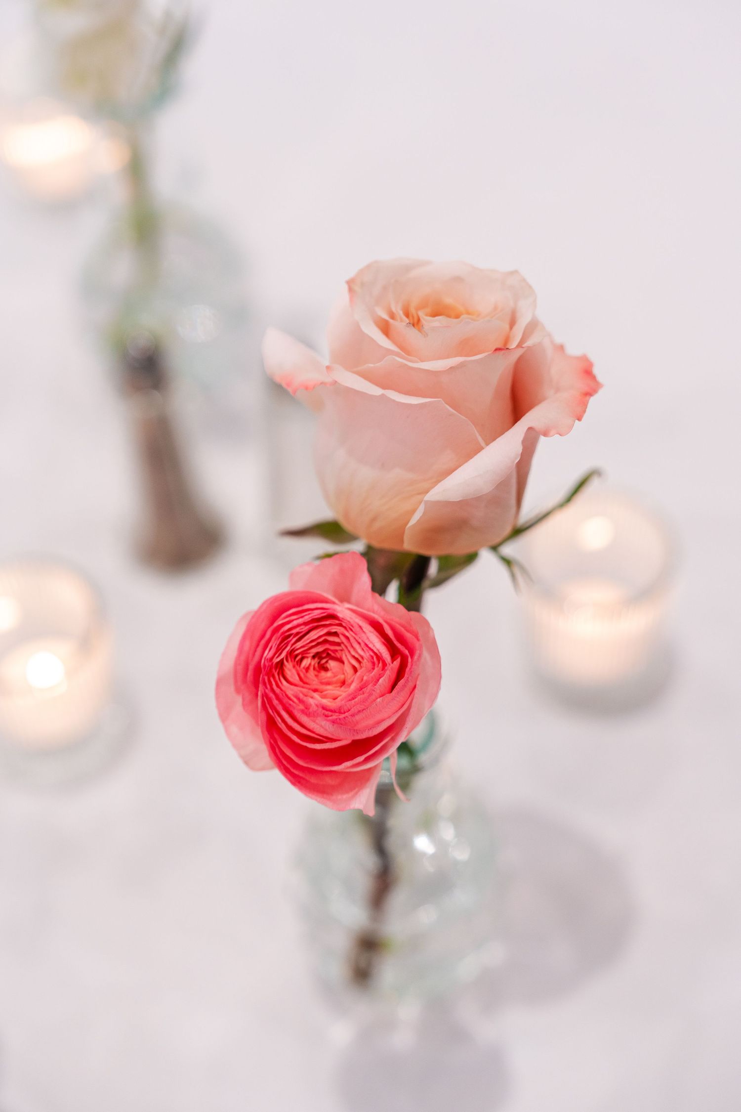 Elegant pink and coral roses in glass vases with soft candlelight bokeh in the background.