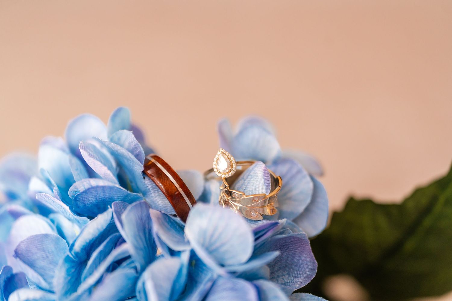 Wedding ring set featuring pear diamond gold ring and wood inlay band nestled in blue hydrangea flowers.