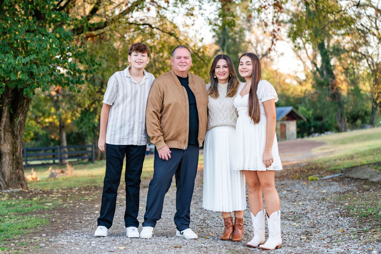 Family of four posing together on a gravel path surrounded by autumn trees at dusk.