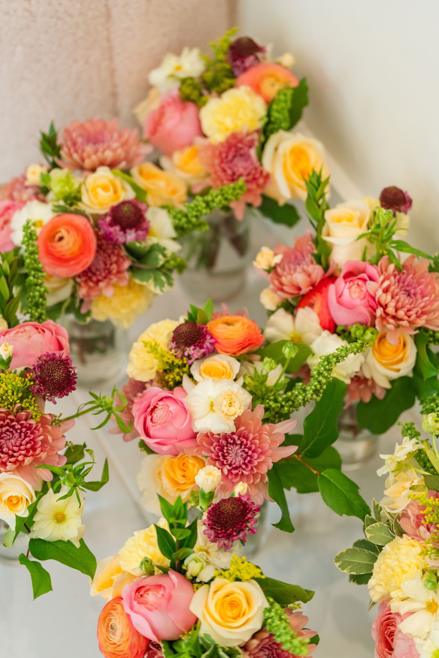 Multiple colorful bridal bouquets with pink dahlias, orange ranunculus, and yellow roses arranged together.