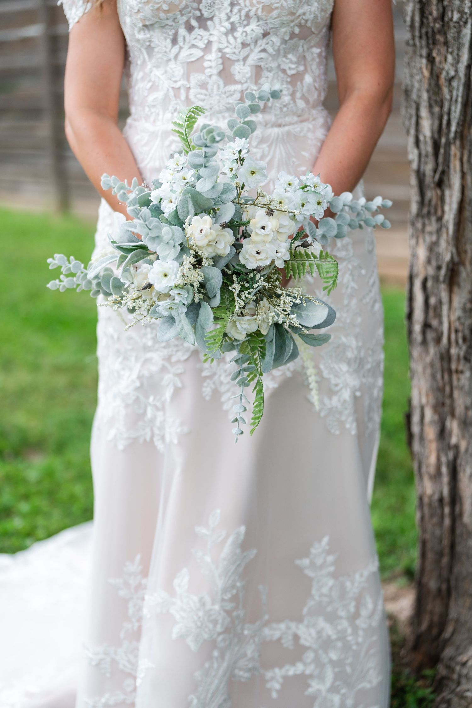 Bride in lace wedding gown holding a white and sage green eucalyptus bridal bouquet.