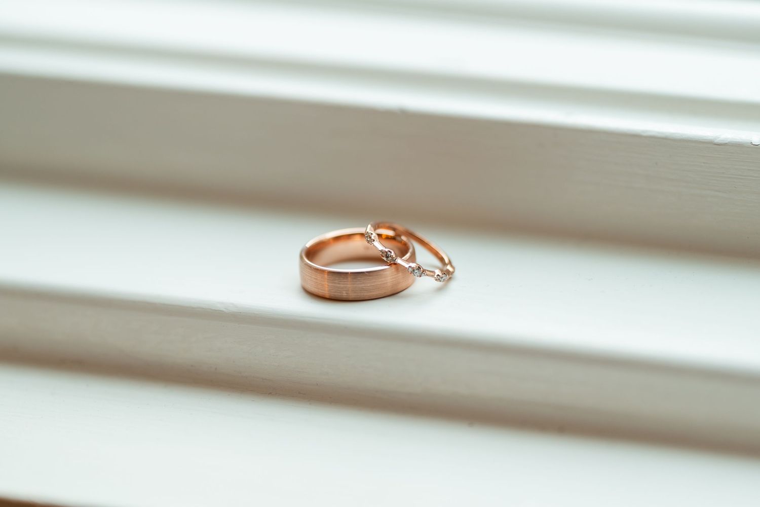 Two rose gold wedding bands resting together on white wooden surface in soft natural light.