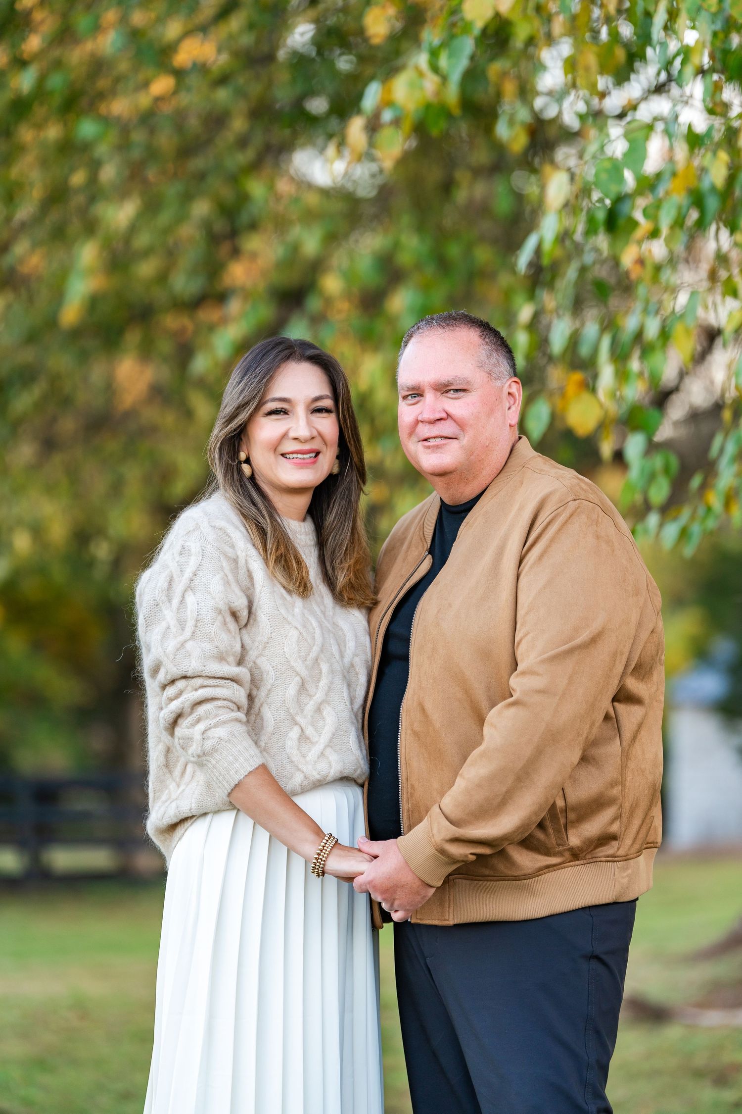 Smiling couple holding hands outdoors under colorful autumn foliage in a park setting.