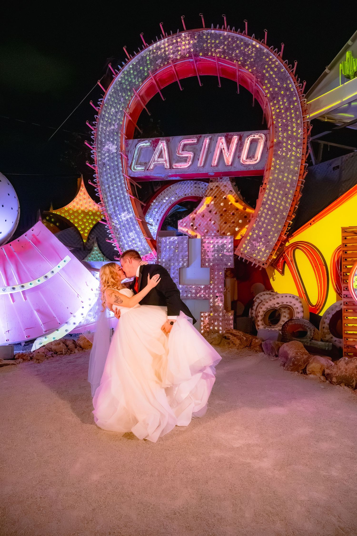 Bride and groom share a romantic kiss in front of a glowing Casino neon sign at the Neon Museum in Las Vegas.