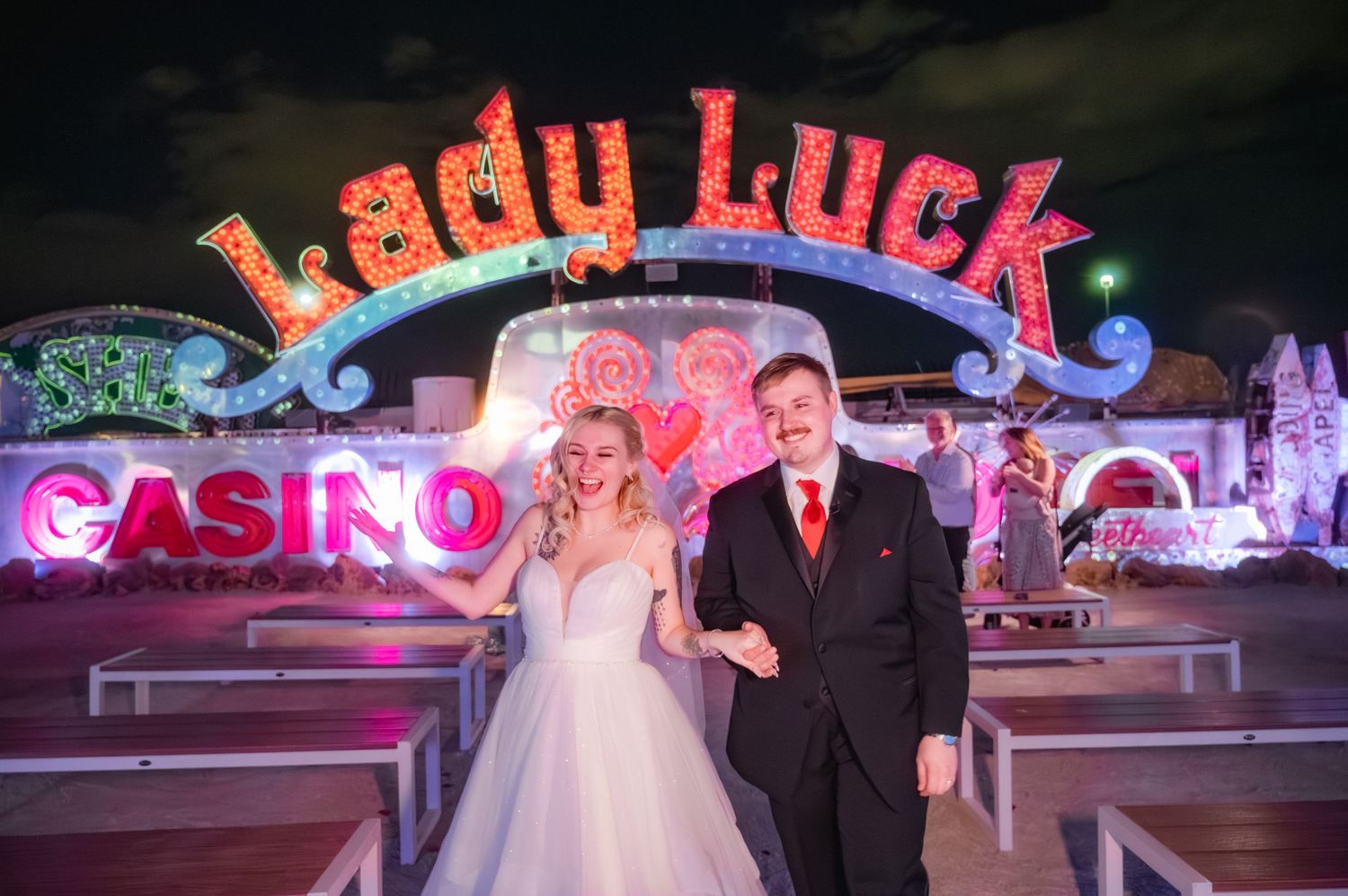Bride and groom posing in front of the Lady Luck Casino neon sign at night in Las Vegas.