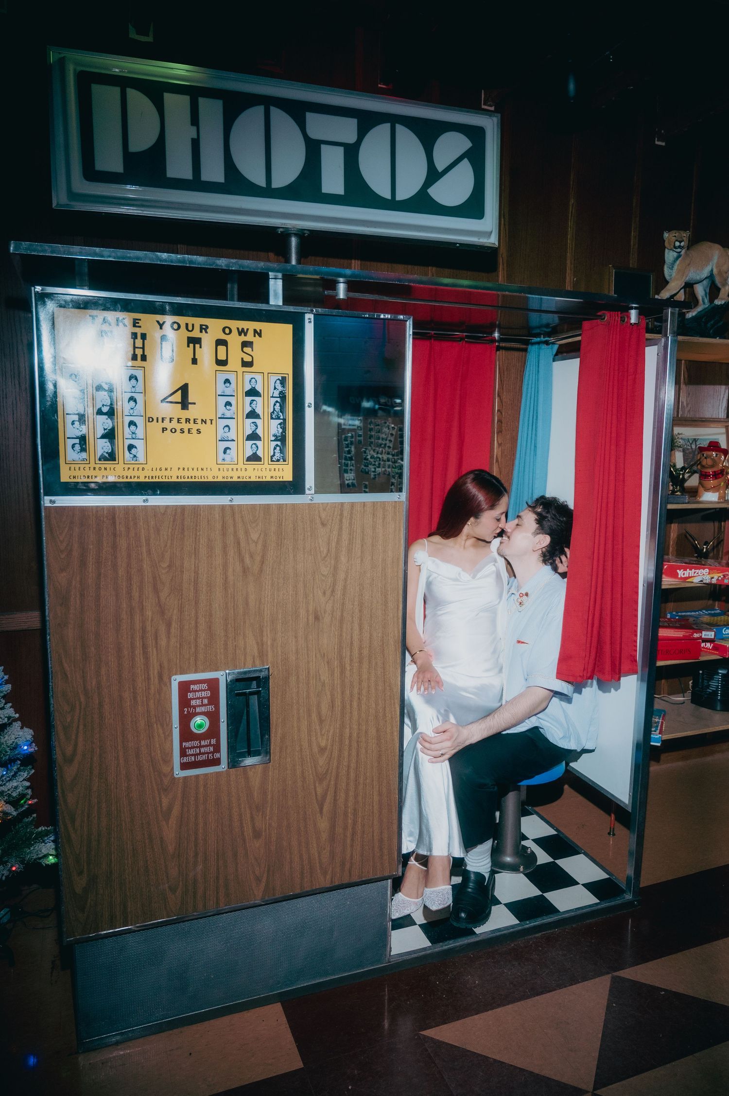 Couple kissing in a vintage photo booth with red curtain and Photos sign at a retro bar in vgeas