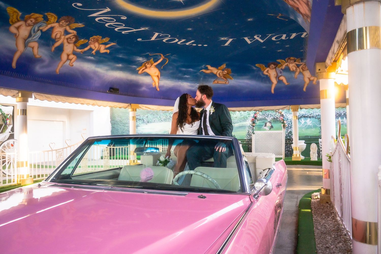 Couple kissing in a pink convertible Cadillac at a Las Vegas wedding chapel with angel mural ceiling.