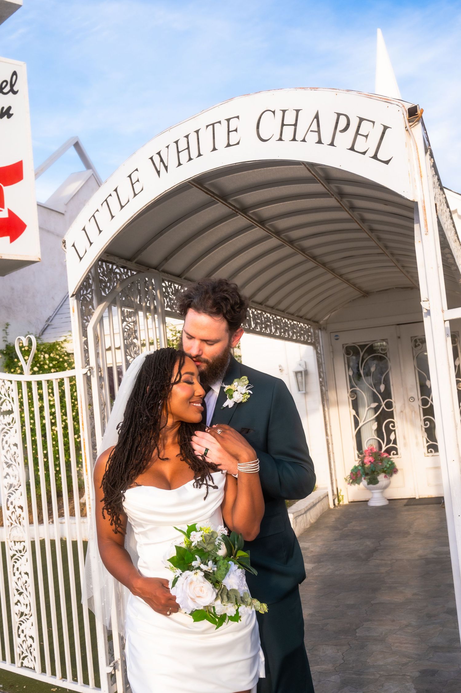 couple embracing at the Little White Chapel in Las Vegas, bride holding white roses bouquet in wedding dress.