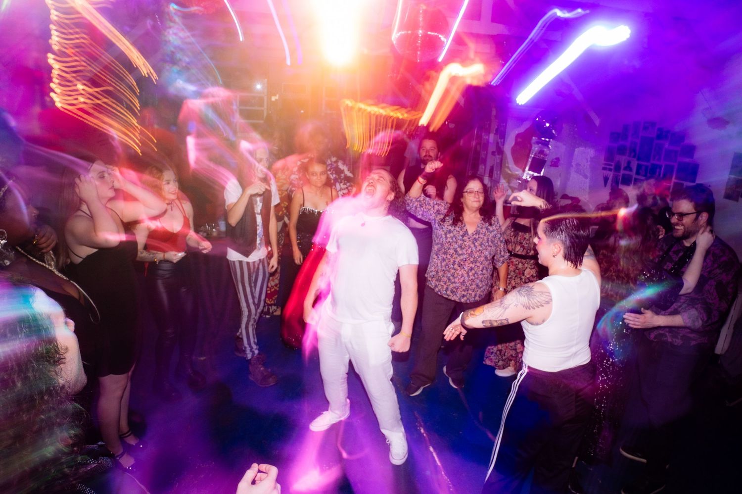 Energetic reception dance floor with colorful purple and pink lights illuminating a crowd of guests
