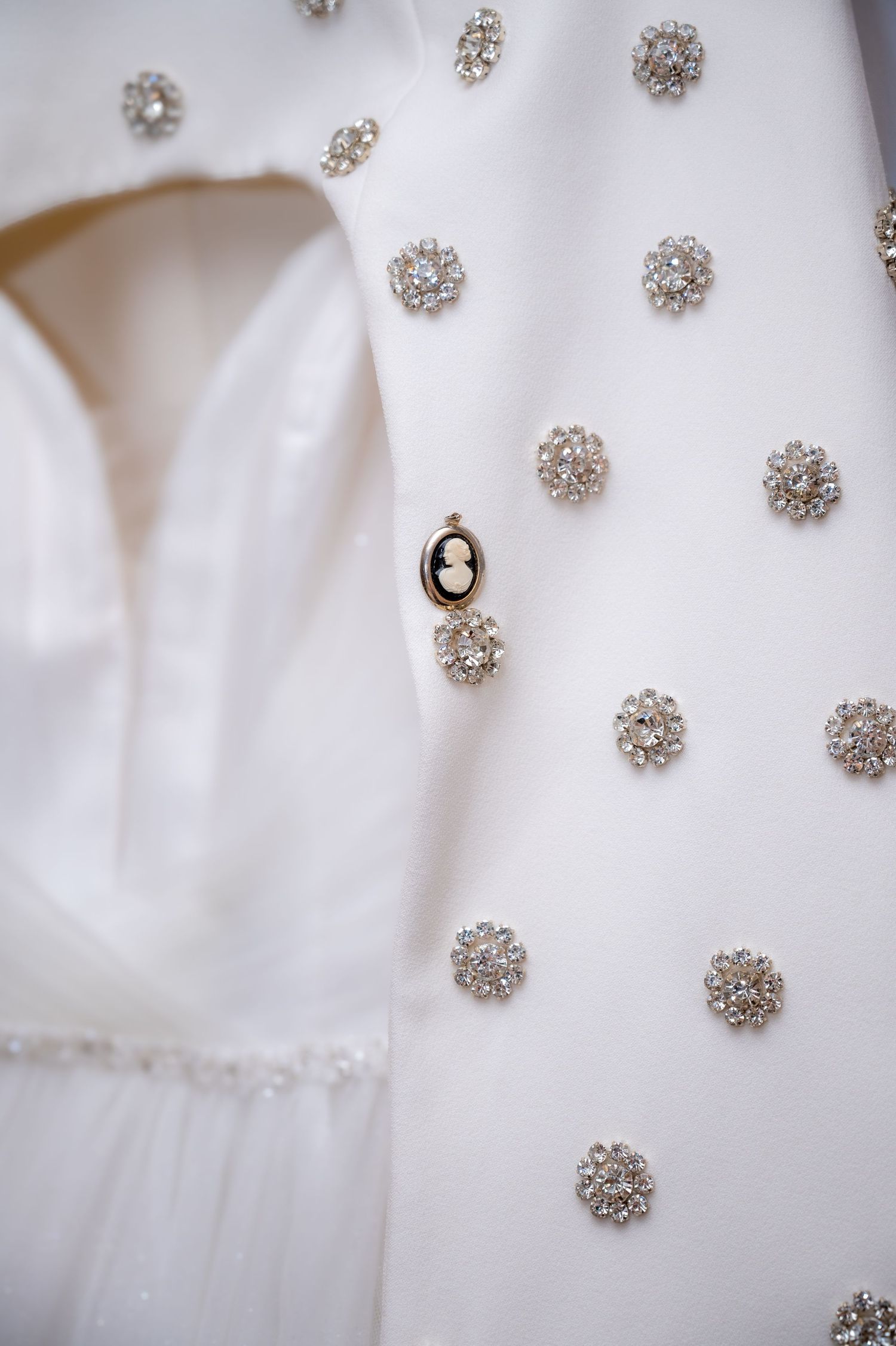 White wedding dress adorned with crystal rhinestone floral embellishments and a delicate cameo brooch detail.
