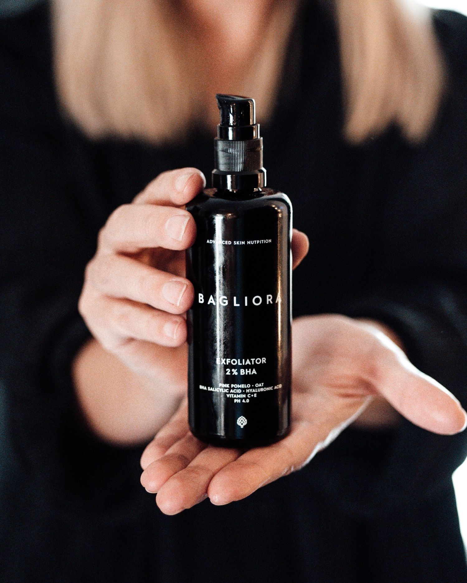 Woman holding a dark glass bottle of Bagliora 2% BHA exfoliator skincare product.