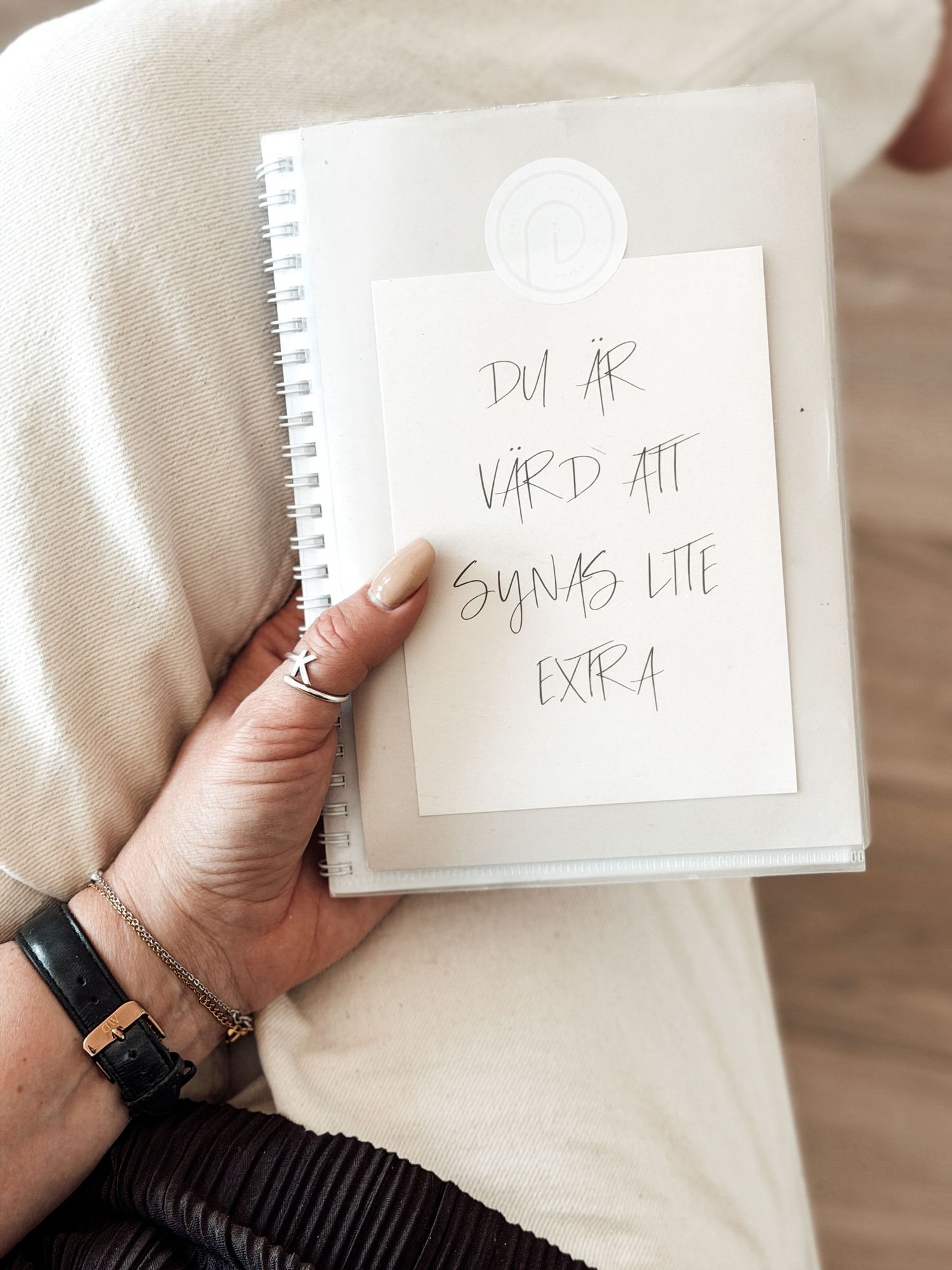 Hand holding a spiral notebook with Swedish text reading du ar vard att synas lite extra written on paper.