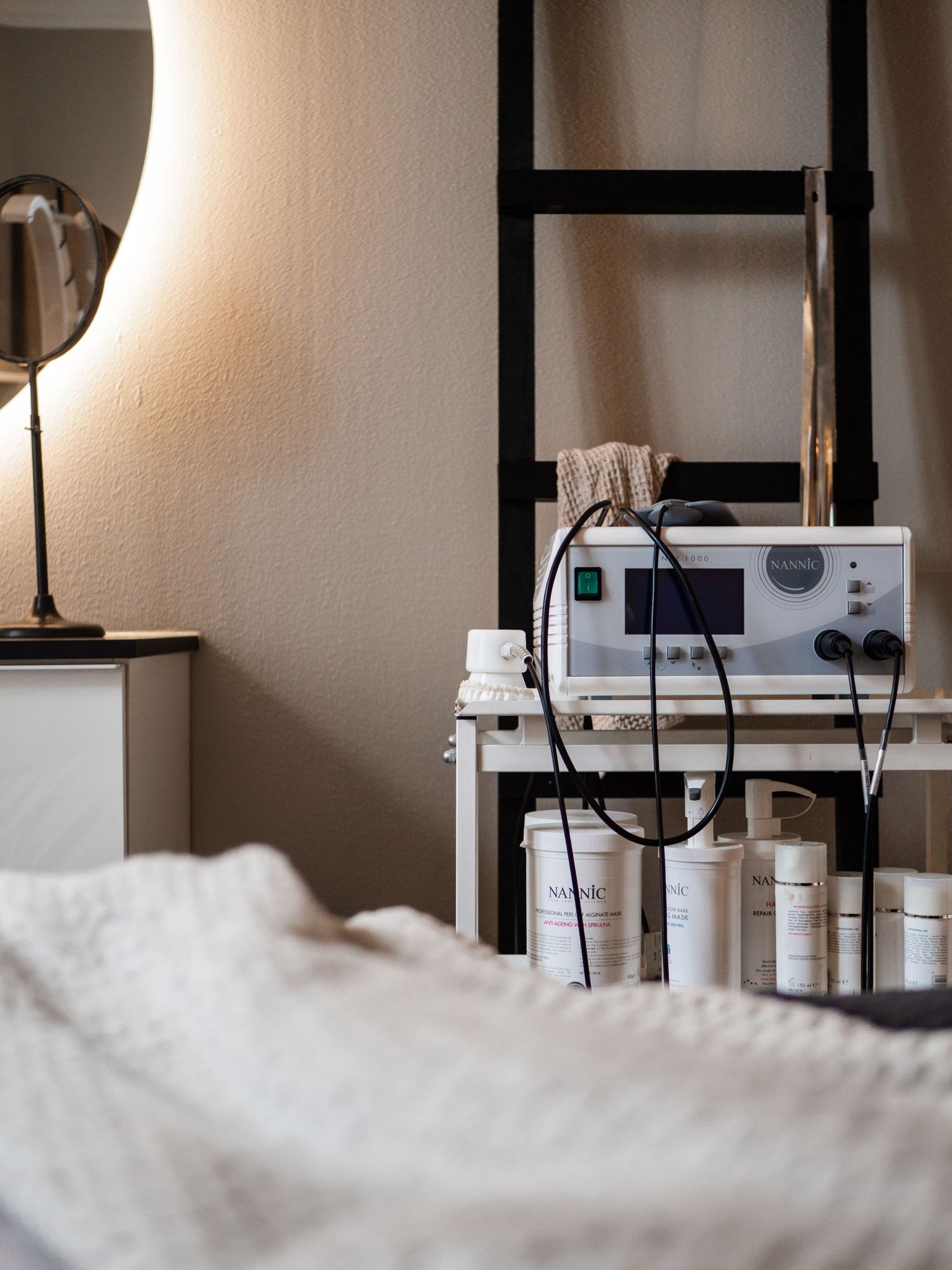 Cozy bedroom corner with skincare machine, products, and warm lamp beside a ladder shelf.