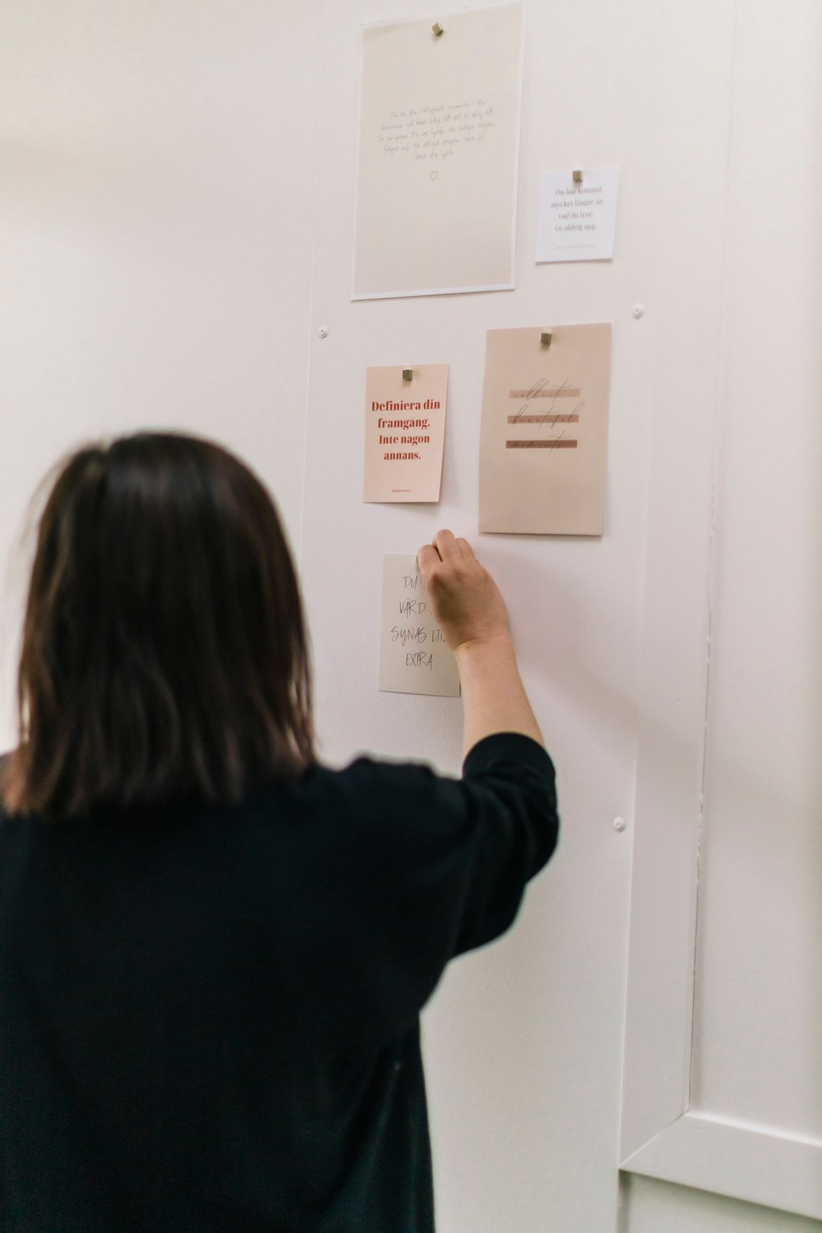 Woman in black sweater pinning cards and notes to a white office inspiration board wall.