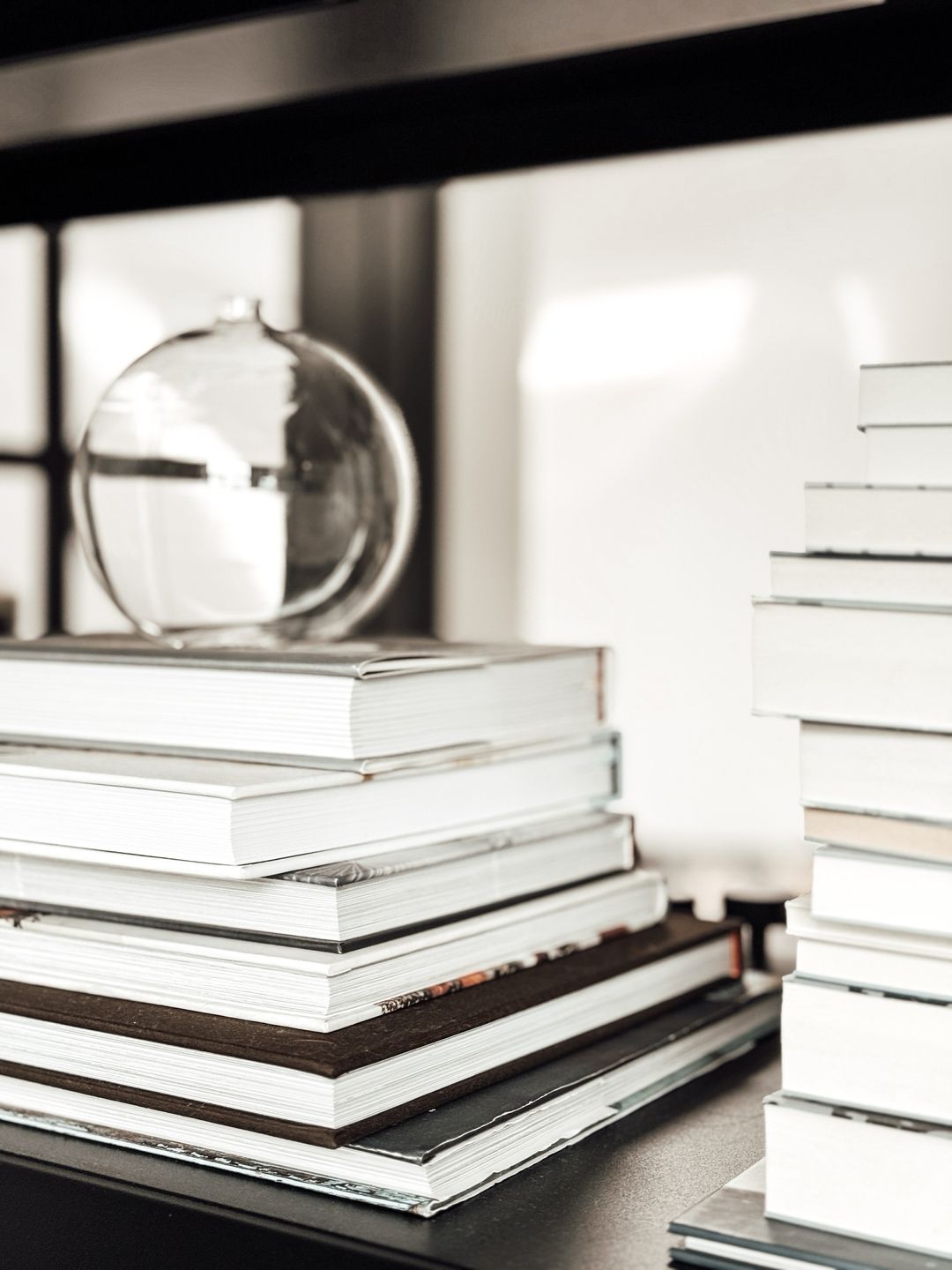 Stacked white hardcover books with a glass globe on a dark shelf in a modern minimalist interior.
