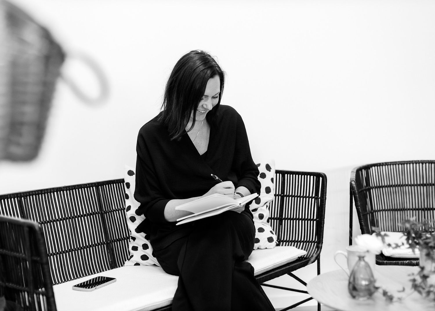 Elegant woman in black dress writing in notebook while seated in modern outdoor patio setting.