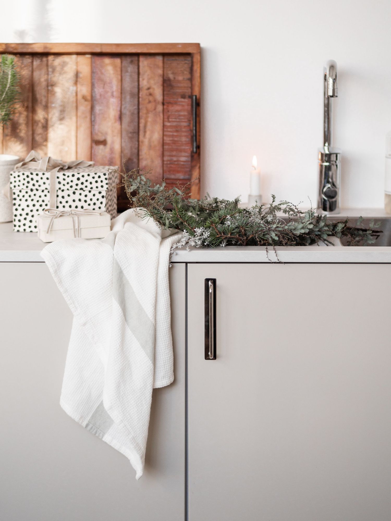 Minimalist white kitchen counter with green garland, candle, and rustic wooden backdrop.