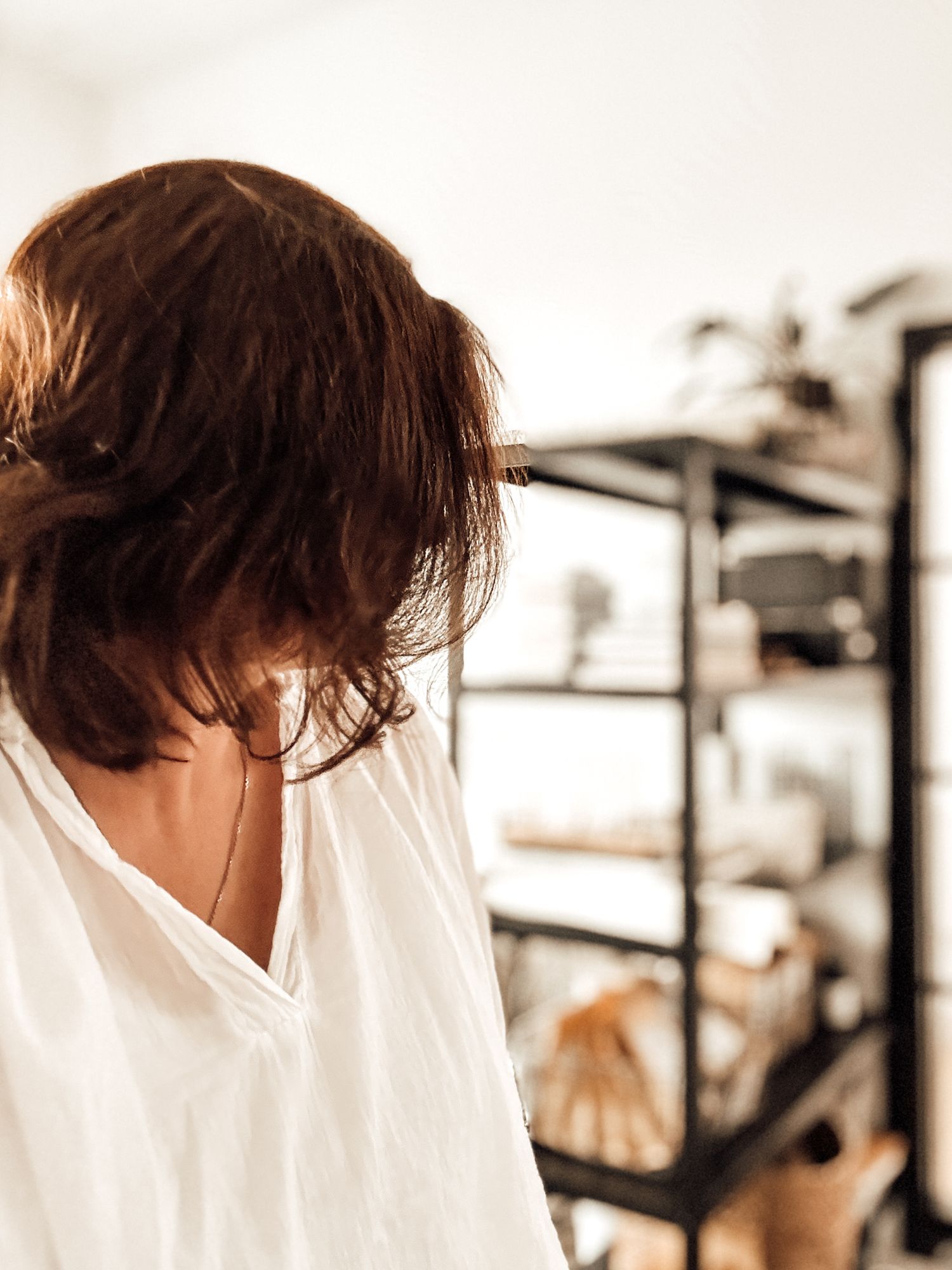 Woman with brown updo hair in white blouse standing near black metal shelving unit.