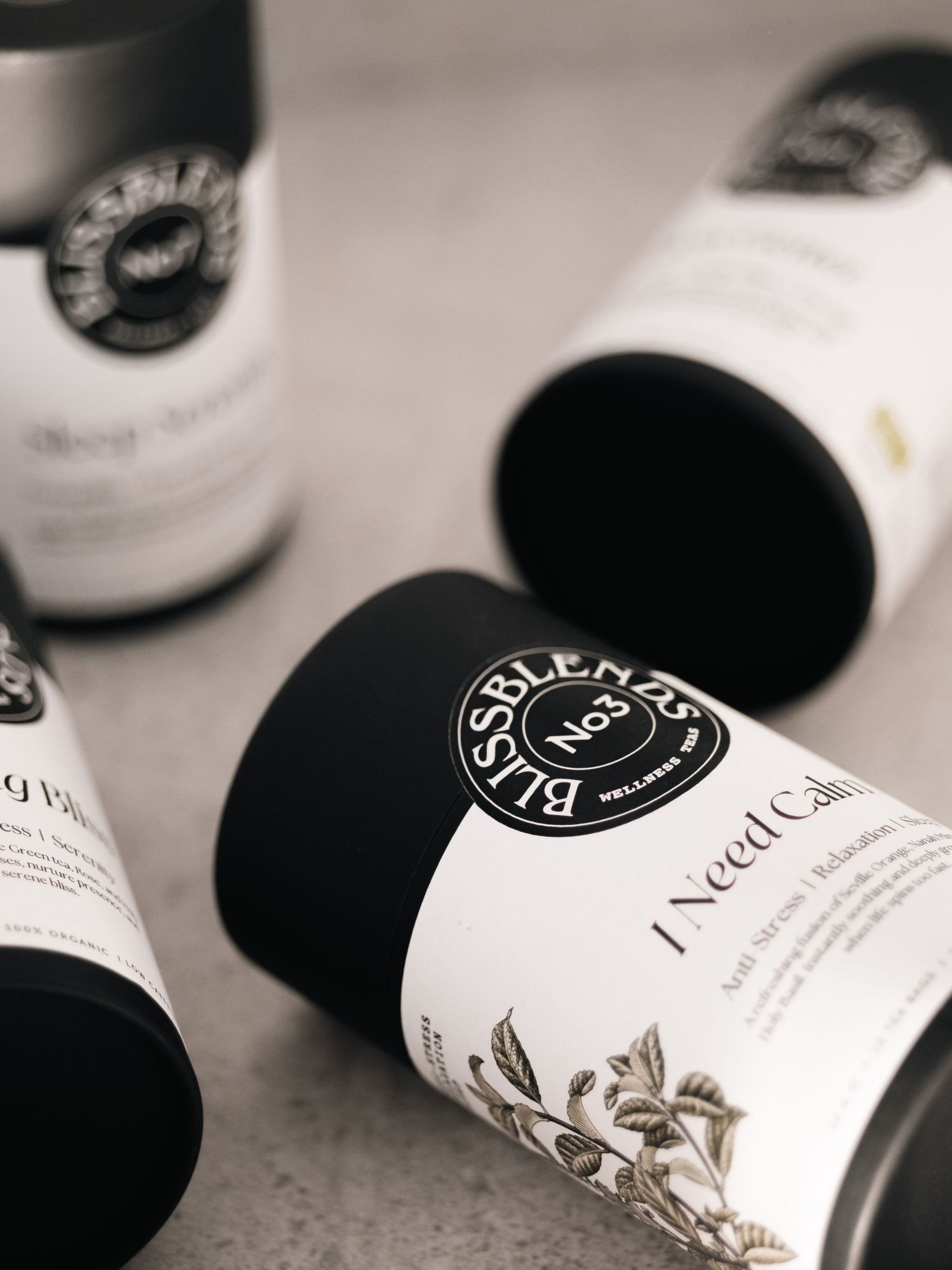 Black and white cylindrical BLISSBLENDS wellness supplement containers arranged on a gray surface.