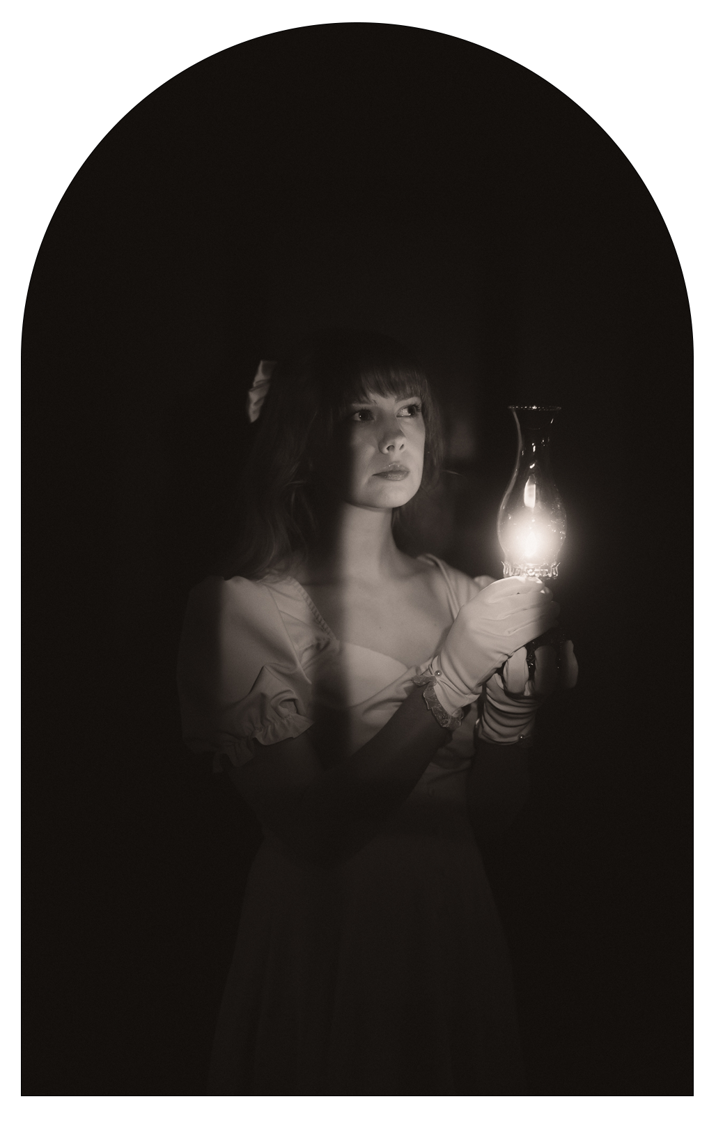 Black and white photo of central Michigan photographer Lynzee Harrison holding an oil lamp in a dark room.
