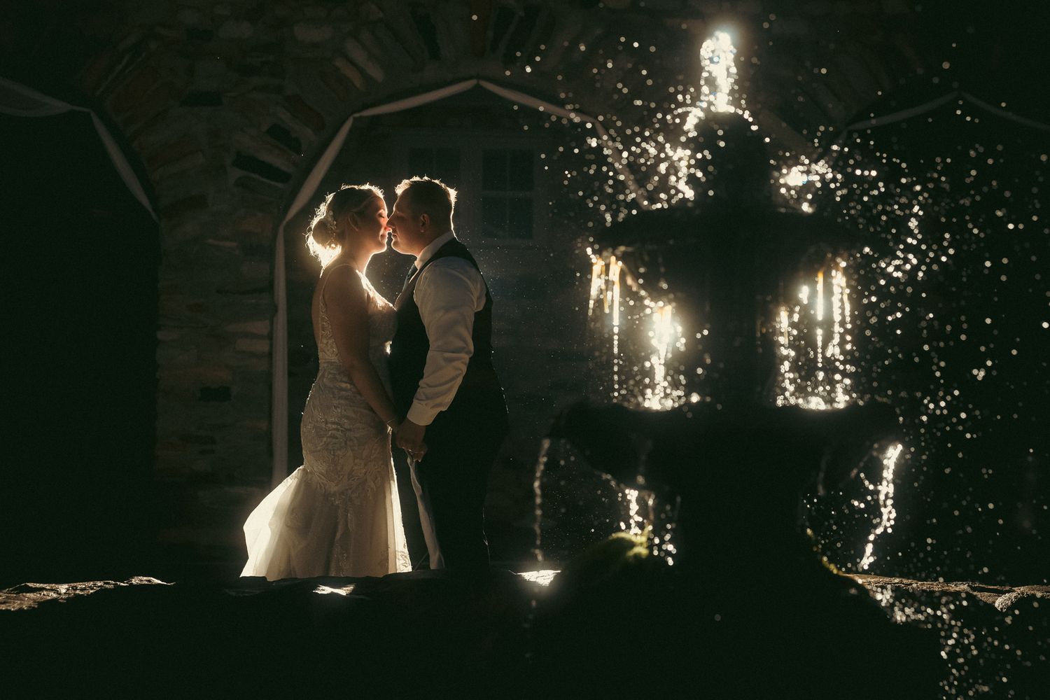 A couple shares a romantic kiss at night surrounded by sparklers creating a magical wedding photography moment.