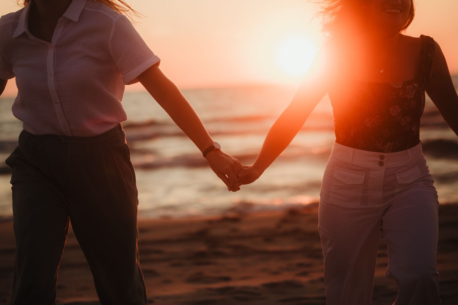Couple walking on beach at sunset holding hands in romantic scene.