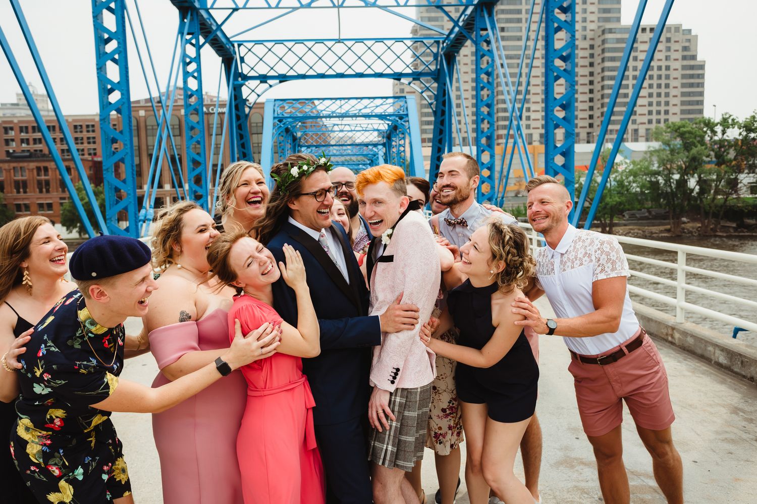 Wedding party poses on blue steel bridge during outdoor celebration.