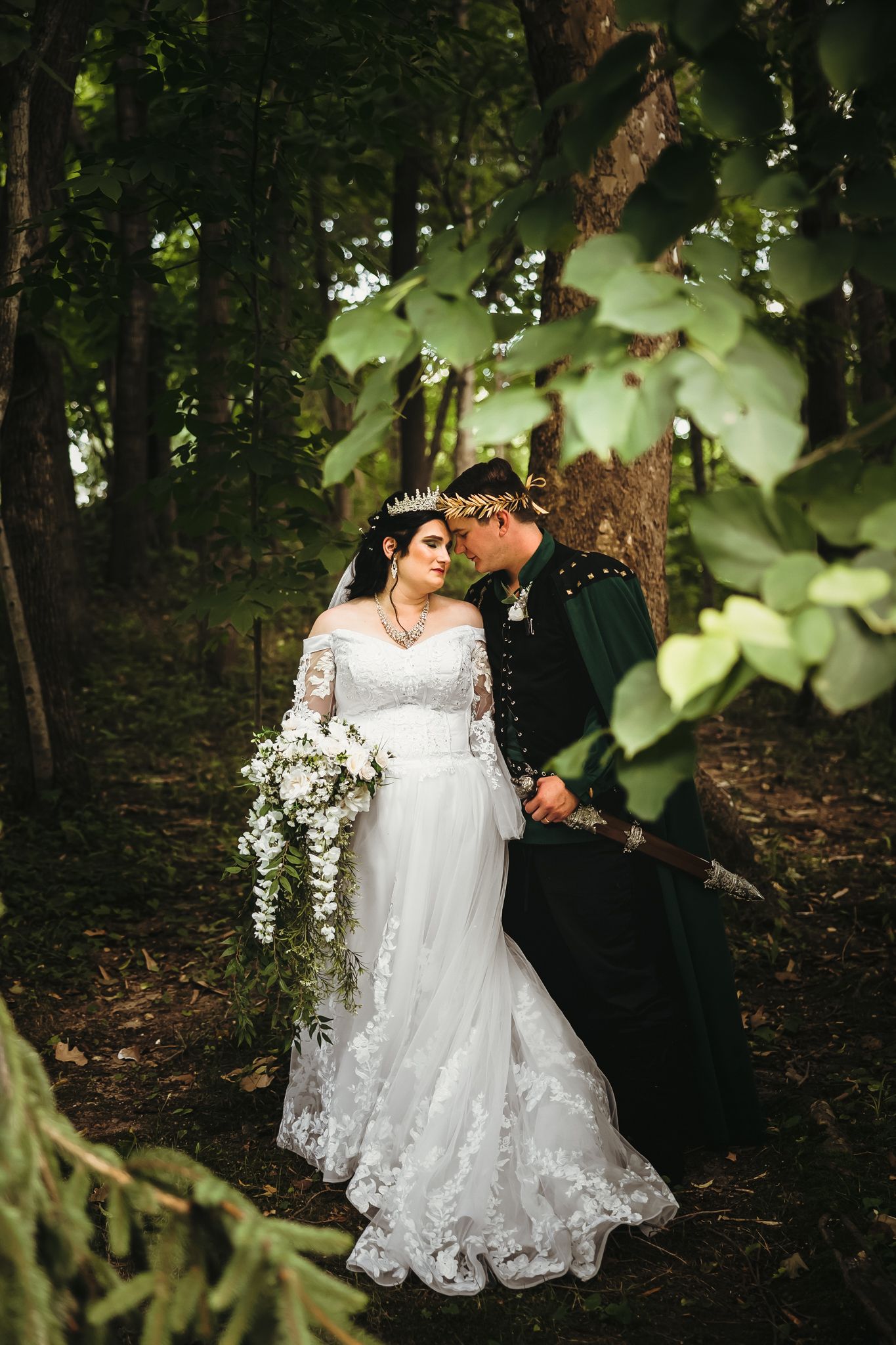 Couple in wedding attire poses among lush greenery in forest setting.