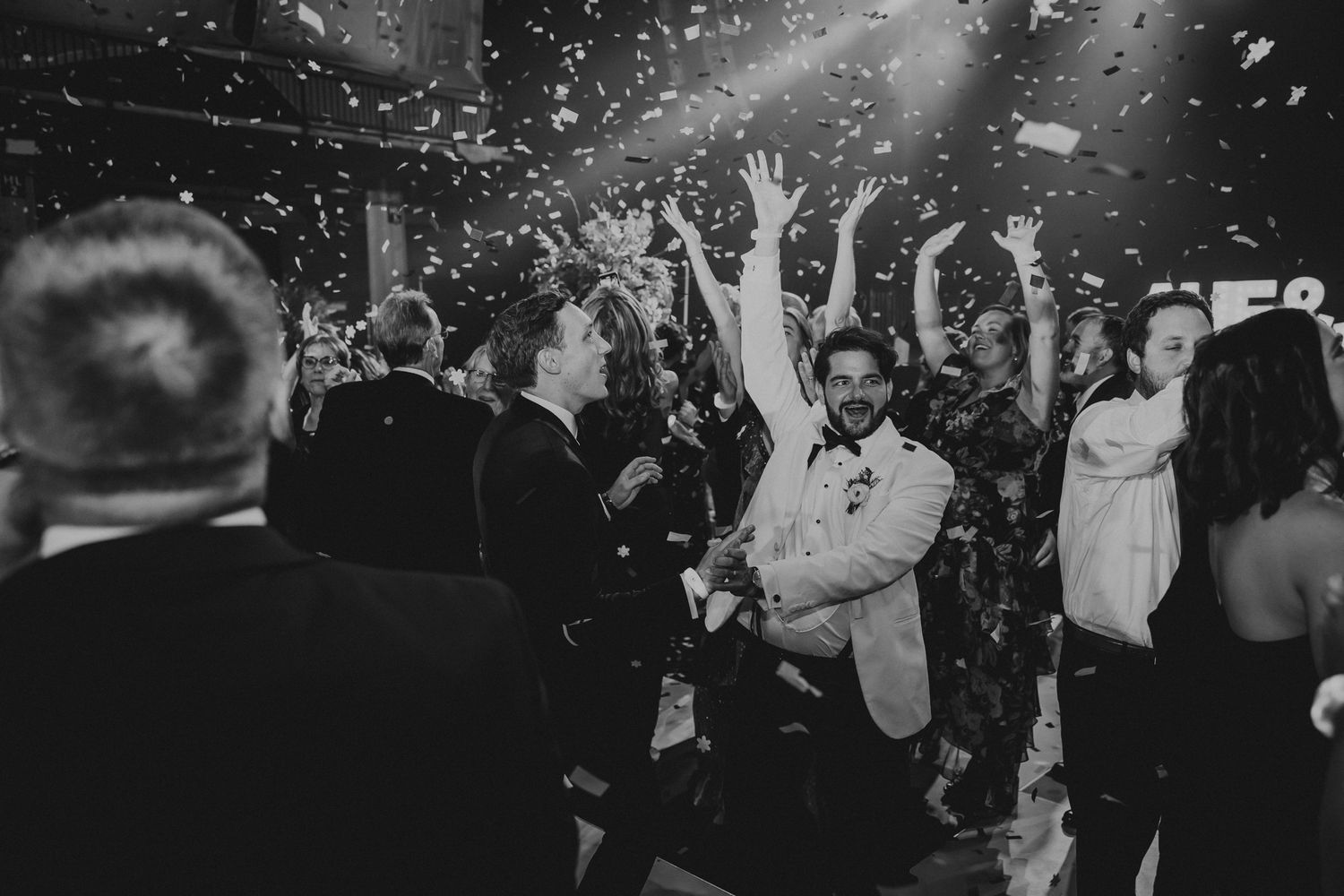 Wedding party celebrates on dance floor with confetti and sparklers in candid moments of joy.