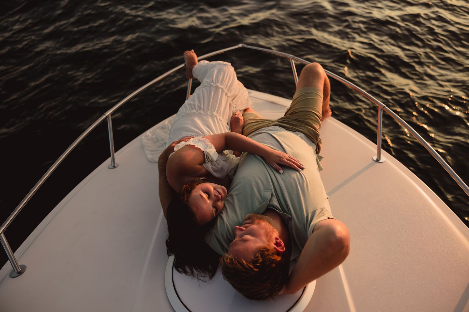 A couple lounges together on a boat deck during golden hour on calm waters.