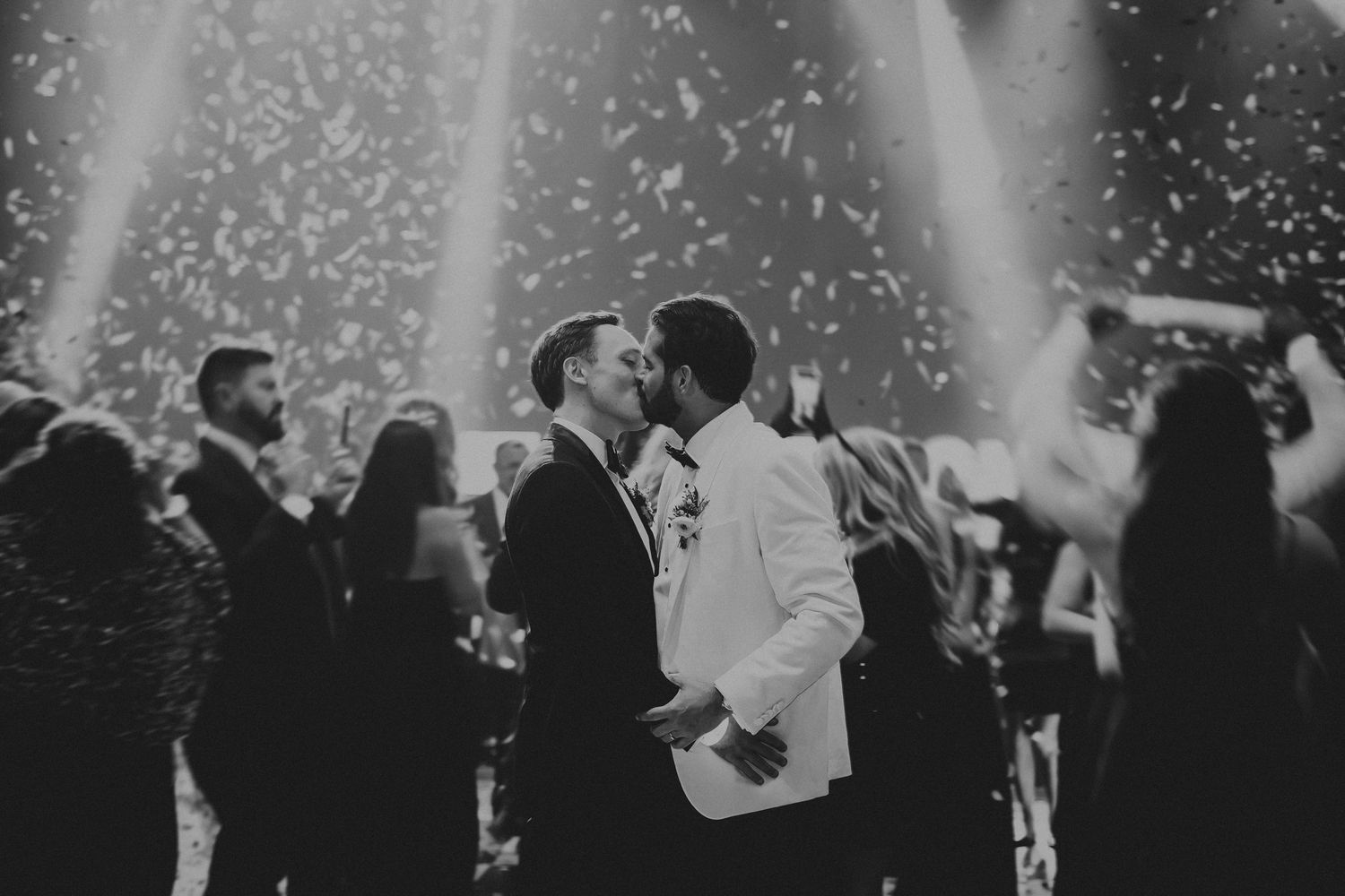 A black and white photo of a couple dancing at a wedding reception with falling confetti and dramatic spotlights.