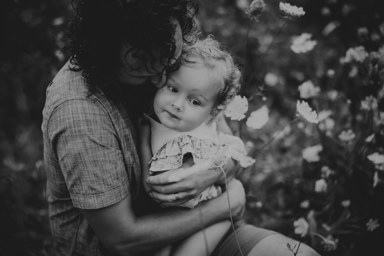 A black and white collage of intimate family moments captured among blooming flowers in a garden setting.