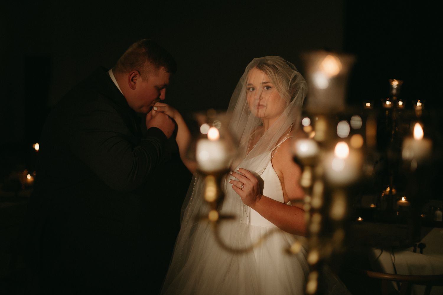 A couple shares an intimate dance moment at a candlelit wedding reception with warm glowing lights in the background.