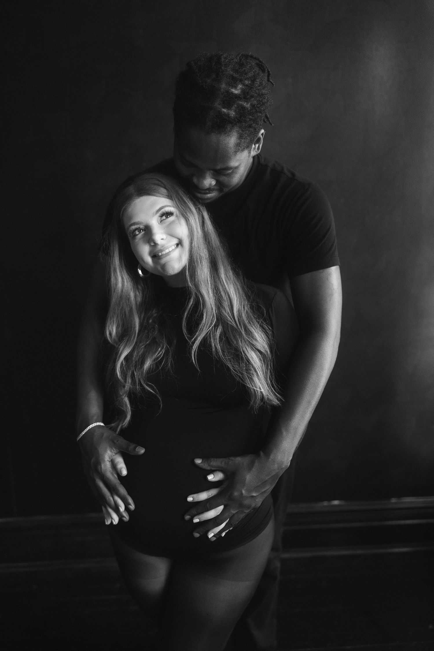 A romantic black and white portrait of a couple embracing in an intimate pose against a dark background.