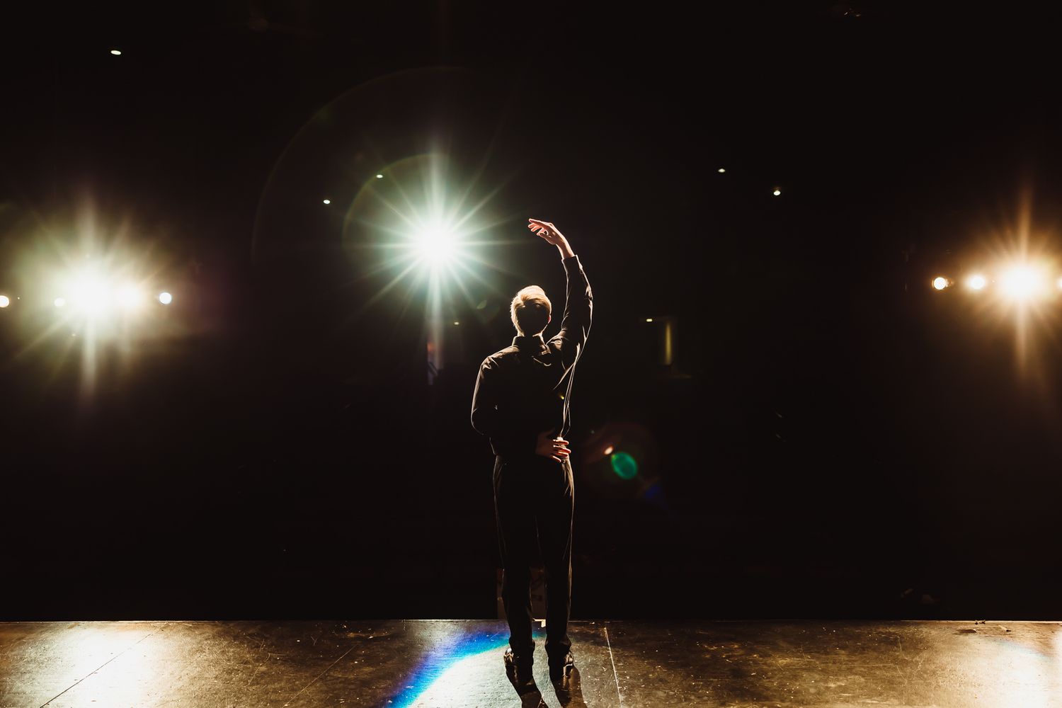 Dramatic silhouette on stage with spotlights in dark theater.