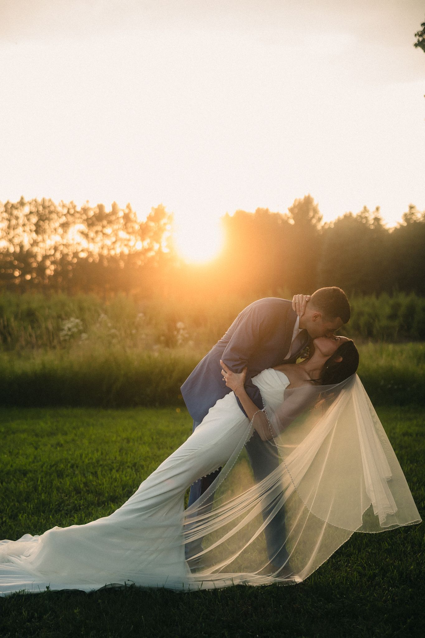 Couple in wedding attire sharing intimate moment at golden sunset in field.