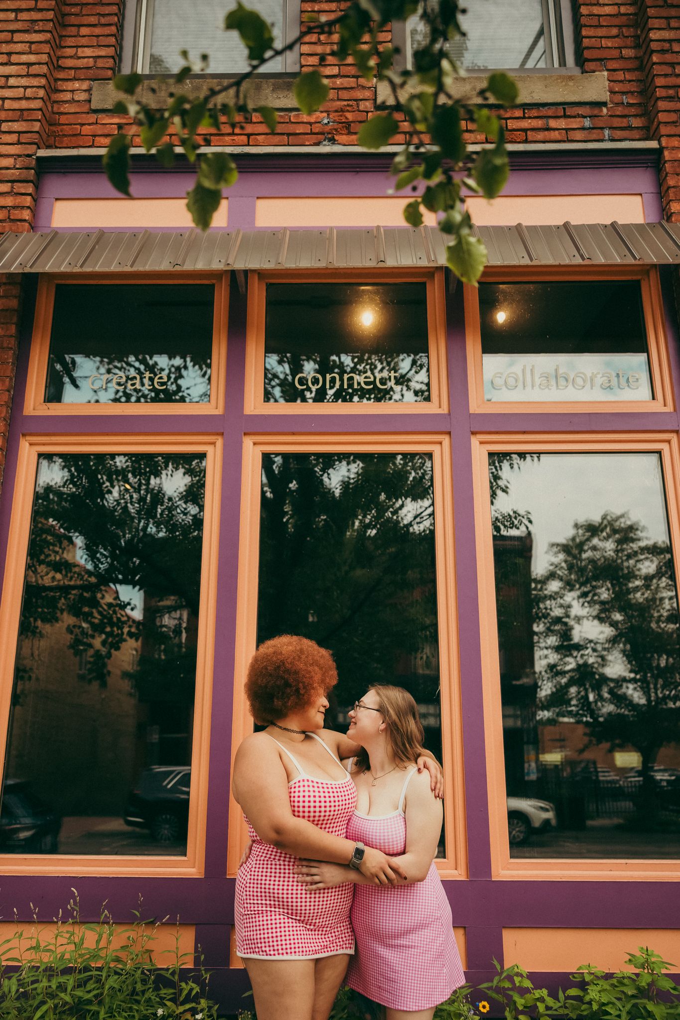 Affectionate couple posing together outside storefront with brick wall and purple accents.